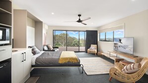 A modern hotel room with a large bed, a TV, a balcony with a view, and a ceiling fan.