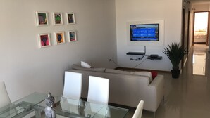 Una sala de estar moderna con una mesa de comedor de vidrio, un sofá blanco y un televisor de pantalla plana montado en la pared.