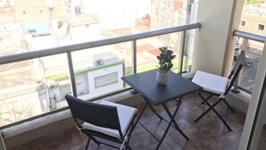 Un balcón con dos sillas, una mesita, una planta en maceta y vistas a edificios.