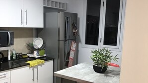 Una cocina compacta con armarios blancos, un refrigerador, un microondas y una pequeña mesa de comedor con dos sillas.