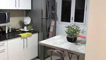 Una cocina compacta con armarios blancos, un refrigerador, un microondas y una pequeña mesa de comedor con dos sillas.