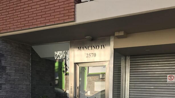 A building with a stone facade and a metal shutter door. The sign above the door reads "MANCINO IV 2570".