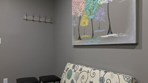 Una habitación con una pared gris, un sofá de tapicería floral, una mesa de centro negra y un cuadro con árboles coloridos.