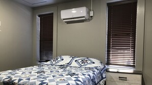 Un dormitorio con cama, mesita de noche, cómoda y aire acondicionado.