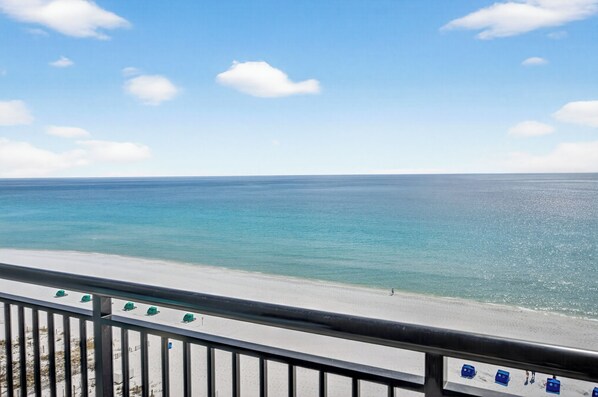 A beach view with a railing, clear sky, and calm sea.