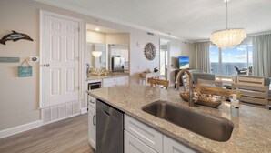 A modern kitchen with a granite countertop, stainless steel sink, and a wooden dining table. - Regency Isle 904 by Liquid Life (Orange Beach)