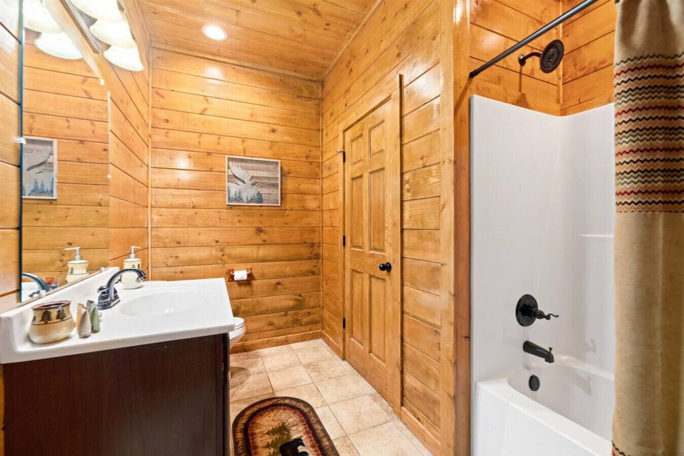 A wooden-paneled bathroom with a sink, mirror, and shower.