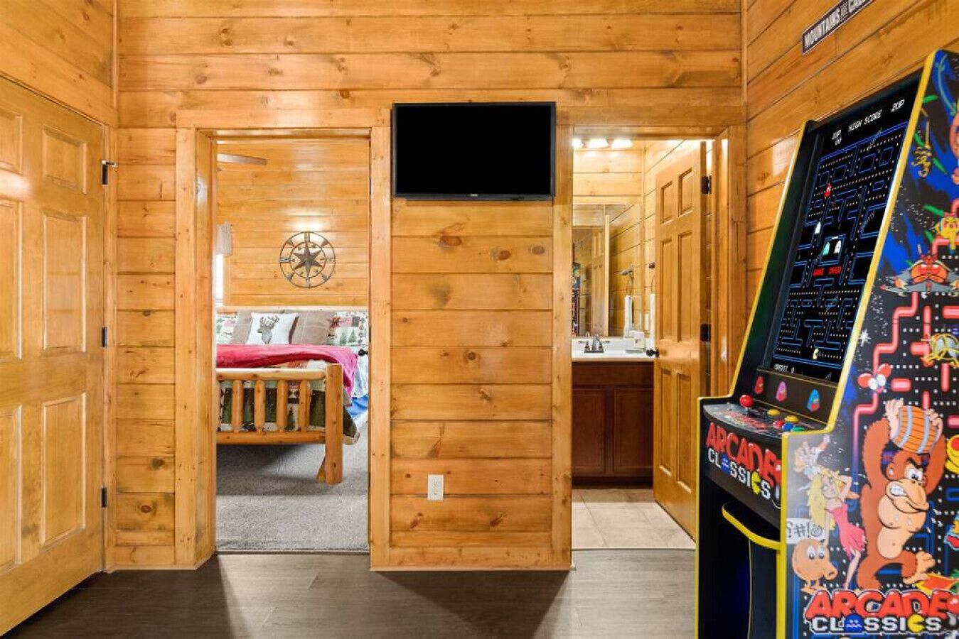A wooden interior with a bed, a television, and an arcade game machine.