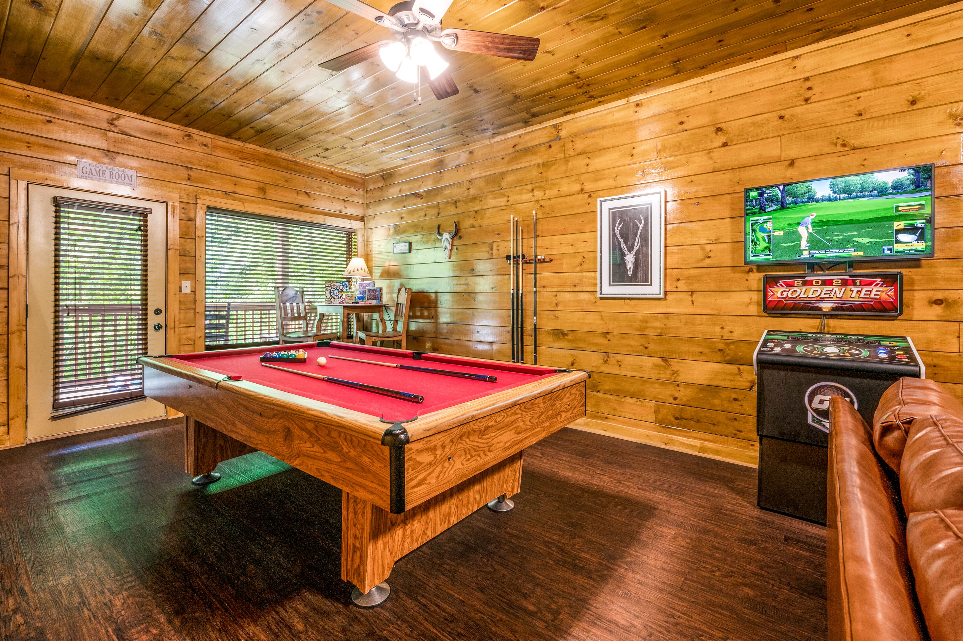 Une table de billard dans une pièce aux murs en bois et dotée d’un ventilateur de plafond.