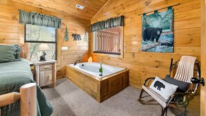 Um quarto de cabana acolhedor, com uma cama, uma mesinha com abajur, uma banheira de madeira e uma cadeira de balanço.