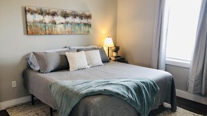 A bedroom with a bed, pillows, a lamp, a painting, and a window. - Bourbon Country Cottage <br>Newly renovated  in the country with amazing views (Mount Eden)