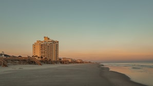 Un hotel frente al mar con un edificio destacado, un paseo marítimo y una vista despejada del océano.
