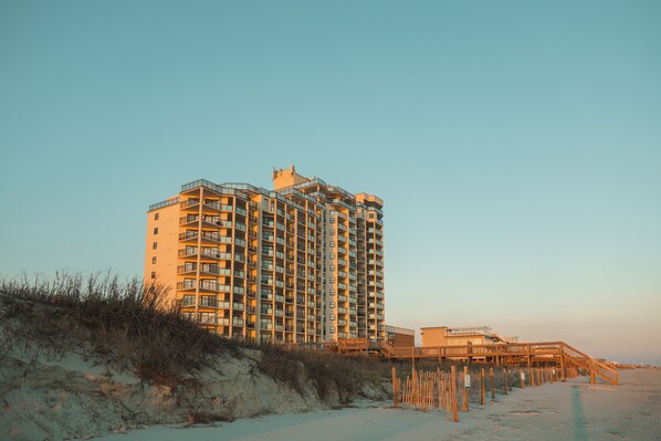 A high-rise hotel with multiple balconies, located near a beach with a wooden walkway leading to the water. - Best views in NC, oceanfront beachfront 3BR 3BA (Ocean Isle Beach)