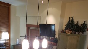 En matplats med ett träbord och stolar, en öppen spis, en tv som är monterad på väggen och ett skåp med dekorativa föremål.