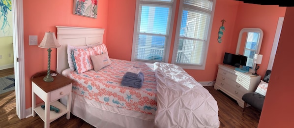 Une chambre à coucher comprenant un lit, une table de chevet, une commode et une fenêtre avec des stores.