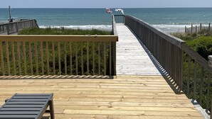 A wooden boardwalk leading to the ocean with a bench and flags.
