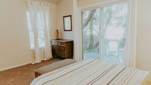 Un dormitori amb un llit, una petita estant, una finestra amb cortines i una porta corredissa de vidre que dona a una zona exterior.