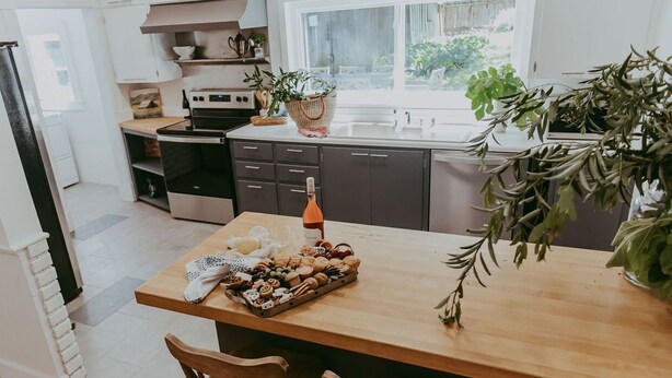 Une cuisine moderne avec un îlot central en bois, des meubles de couleur sombre et une fenêtre agrémentée de plantes.