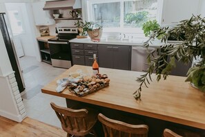 A modern kitchen with a wooden island, dark cabinets, and a window with plants. - The Victorian (Cloverdale)