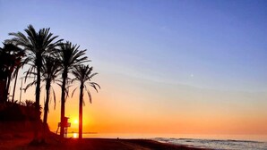 Ein Strand mit Palmen und einem Rettungsturm bei Sonnenuntergang.