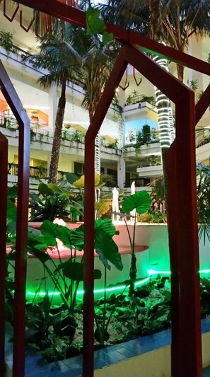 Un atrio de varios niveles con una piscina central, rodeado de abundante vegetación y palmeras.