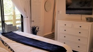 Un dormitorio con cama, cómoda, televisor y puerta con cortinas.