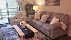 A living room with a sofa, armchairs, a coffee table, a lamp, and a painting on the wall.