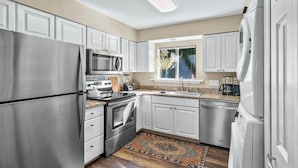 A modern kitchen with stainless steel appliances, white cabinetry, and a window providing natural light.