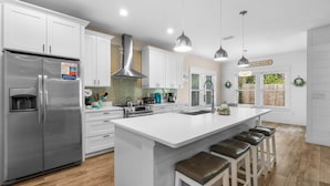 A modern kitchen with white cabinets, stainless steel appliances, and a central island with bar stools.