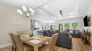 A modern open-plan living area with a dining table, sofas, and a kitchen in the background.