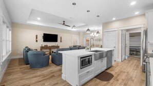 A modern kitchen with a central island, built-in appliances, and a dining area with a gray sofa and a flat-screen TV.