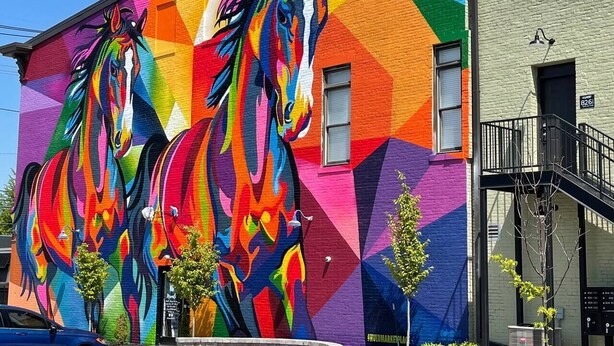 Un edificio con un mural vibrante y colorido de caballos en su fachada.