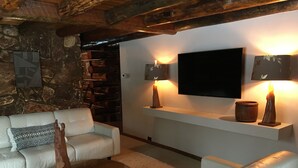 Una sala de estar acogedora con pared de piedra, un televisor de pantalla plana, dos lámparas fijadas a la pared y un sofá blanco.