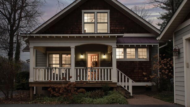 A two-story house with a front porch, a central entrance, and a visible staircase leading to the upper floor.