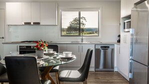 Una cocina moderna con armarios blancos, electrodomésticos de acero inoxidable, una mesa de comedor con sillas y una ventana con vistas al exterior.