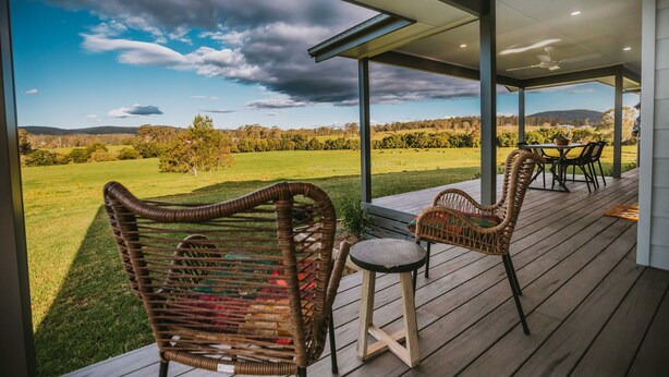 Un espacio al aire libre techado con mobiliario de mimbre y vistas a un campo y colinas.
