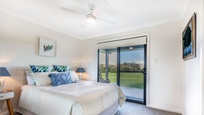 Un dormitorio con cama, lámparas de noche, ventilador de techo y un amplio ventanal corredero que da a un balcón.