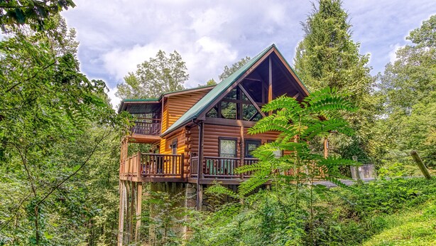 Une cabane en rondins dotée d’un balcon, entourée d’une forêt dense.