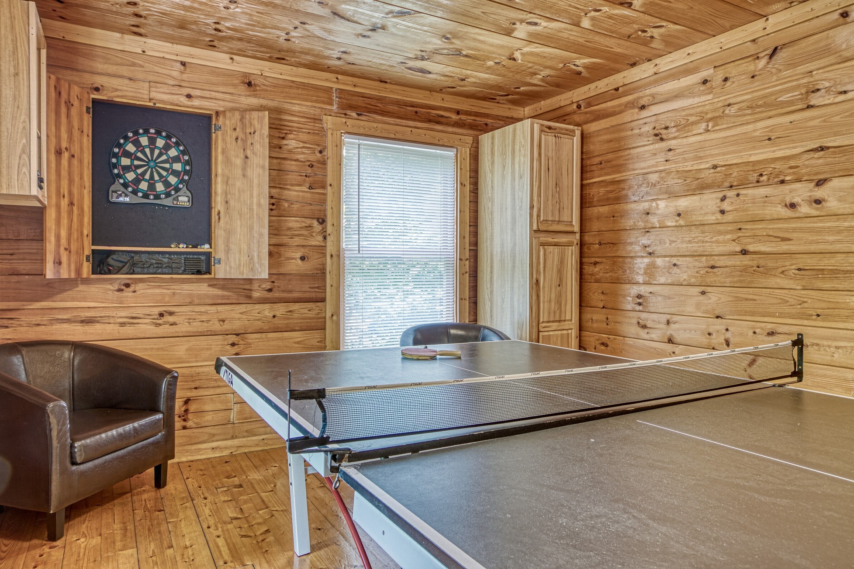 Una mesa de ping pong en una habitación con paredes de madera y un dardo.