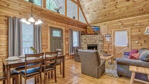 L’intérieur d’un chalet en bois comprend un coin repas, une cheminée et un salon avec un canapé et un téléviseur.