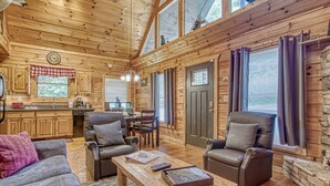 L’intérieur chaleureux d’un chalet en bois comprend un coin repas, deux canapés en cuir, une table basse en bois et une cheminée en pierre.