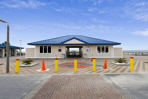 A building with a blue roof and beige walls, featuring a gated entrance, a brick pathway, and bollards.
