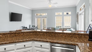 A kitchen with granite countertops, white cabinetry, a built-in dishwasher, and a ceiling fan.