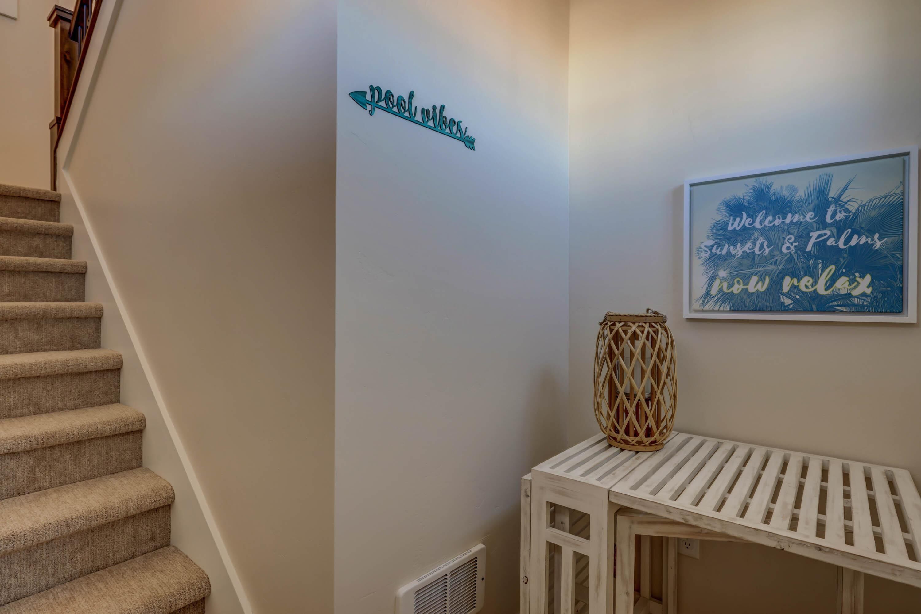 A staircase leading to a landing with a sign that reads "Pool Vibes" and a framed welcome sign with palm trees and the text "Welcome to Sunsets & Palms now relax".