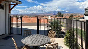 A patio with a round table and wicker chairs, a black metal fence, and a view of a desert landscape with mountains in the background. - Peaceful | Clean | Get-a-way!  | Sunsets and Palms Casita (Washington)