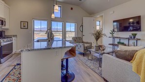 A modern kitchen with a large island, a dining area with a view, and a living room with a sofa and TV. - Peaceful | Clean | Get-a-way!  | Sunsets and Palms Casita (Washington)