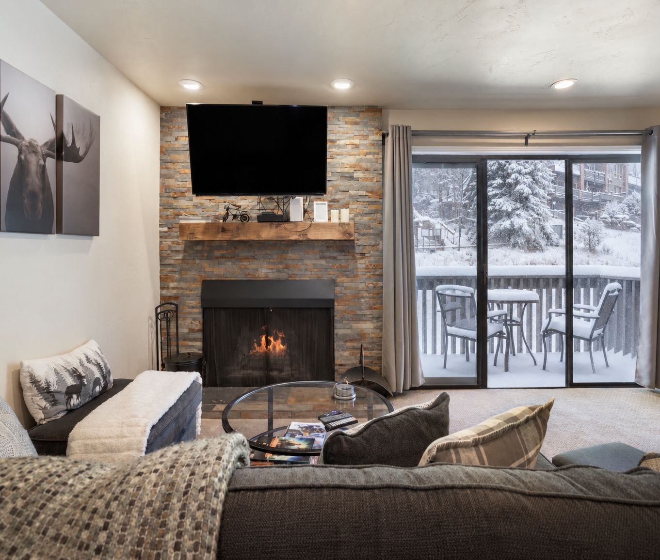 A living room with a fireplace, a television mounted above it, and a balcony with outdoor seating.