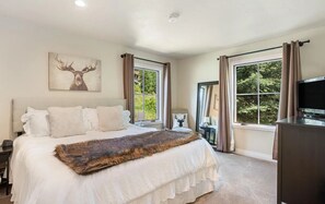 A bedroom with a large bed, a television, and a window with curtains.