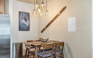 A dining area with a wooden table, chairs, a hanging light fixture, a poster on the wall, and a wooden beam.