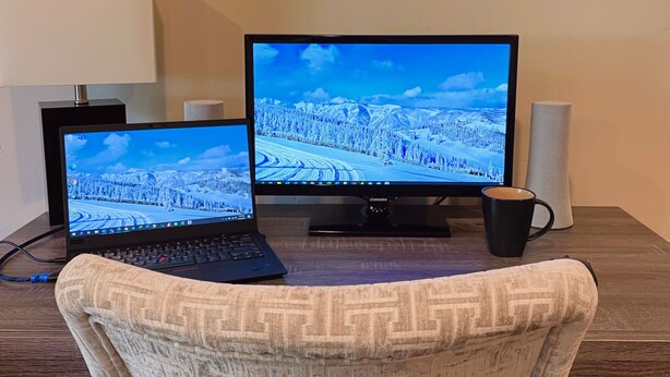 Un escritorio con una laptop y una computadora de escritorio, ambas mostrando un paisaje nevado. Hay una taza de café y un objeto cilíndrico blanco sobre el escritorio.